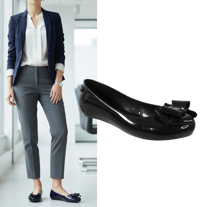 Person wearing a navy blazer and gray pants with black shoes featuring a bow, against a blurred indoor background.