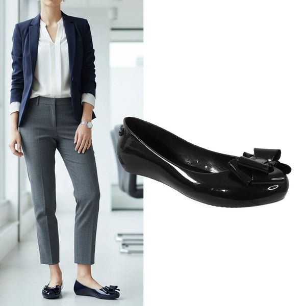 Person wearing a navy blazer and gray pants with black shoes featuring a bow, against a blurred indoor background.